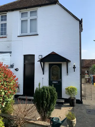 The same cottage elevation repainted in clean white masonry paint, with the timber canopy and doors finished in black and a new green front door.